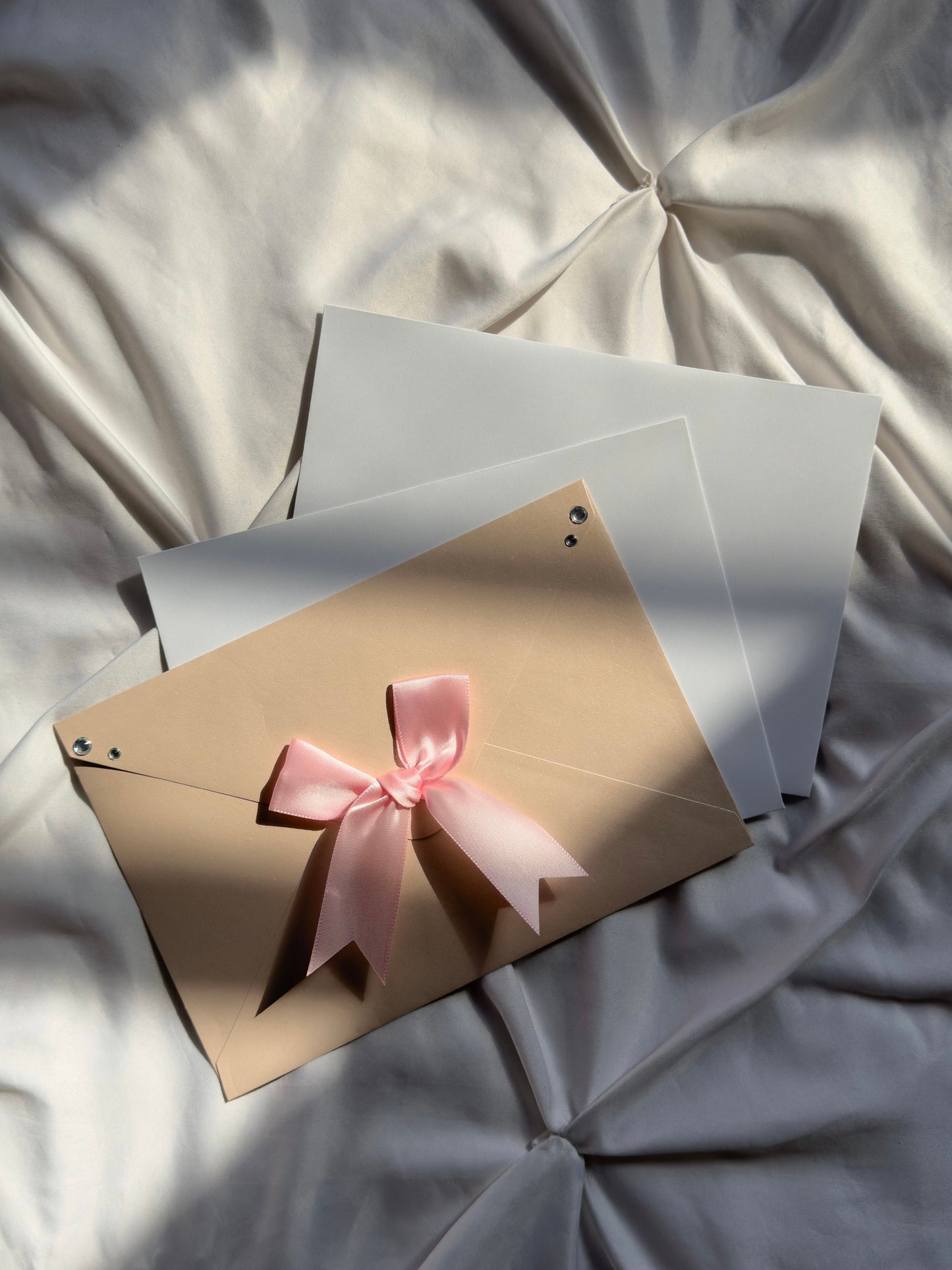 Three envelopes, the one in front pink with a pink bow and silver jewels at corners.