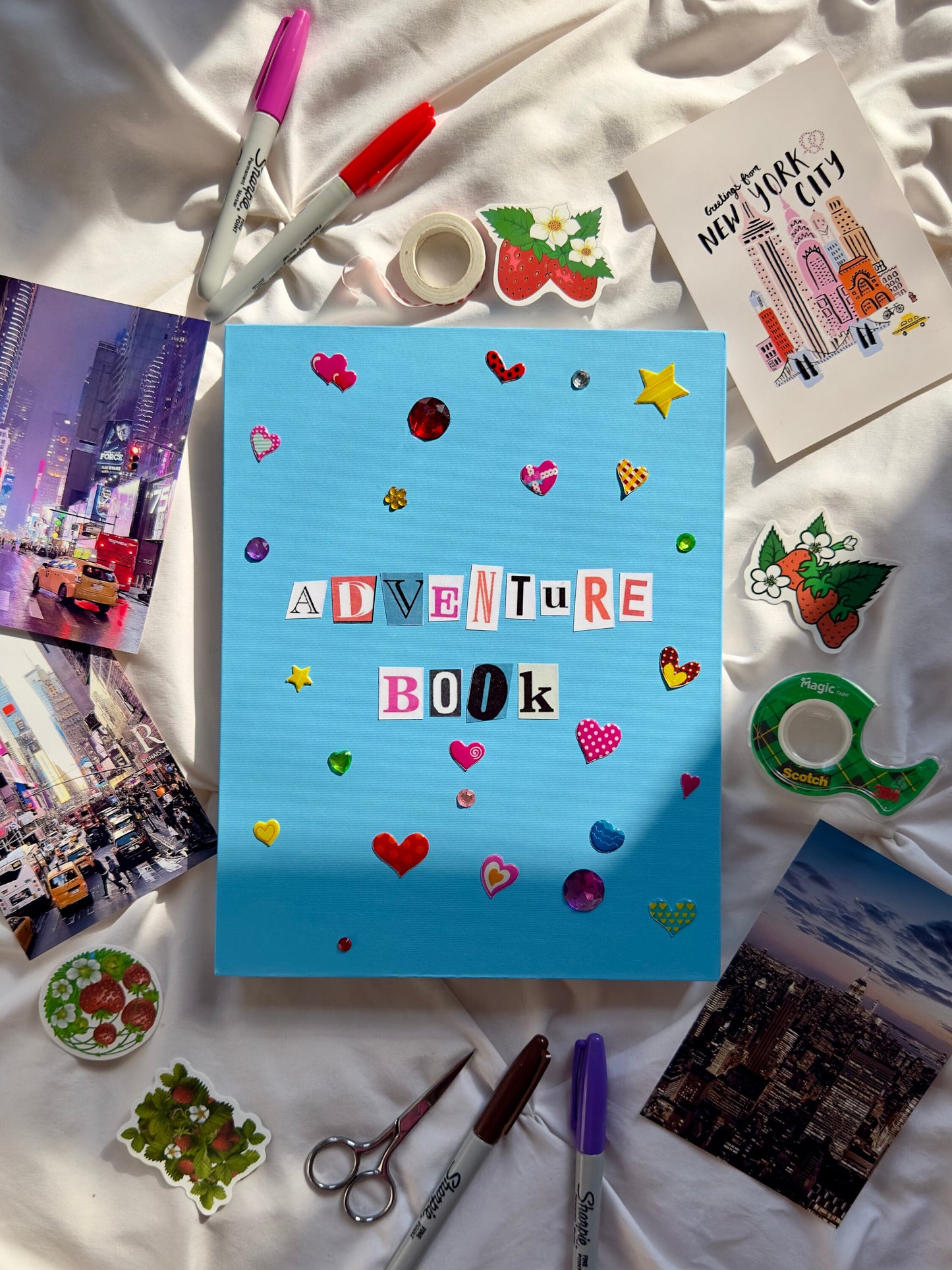 Cobalt blue hardcover scrapbook with “Adventure Book” newspaper letters on the cover. Decorated with multicolored heart and star stickers and jewels.