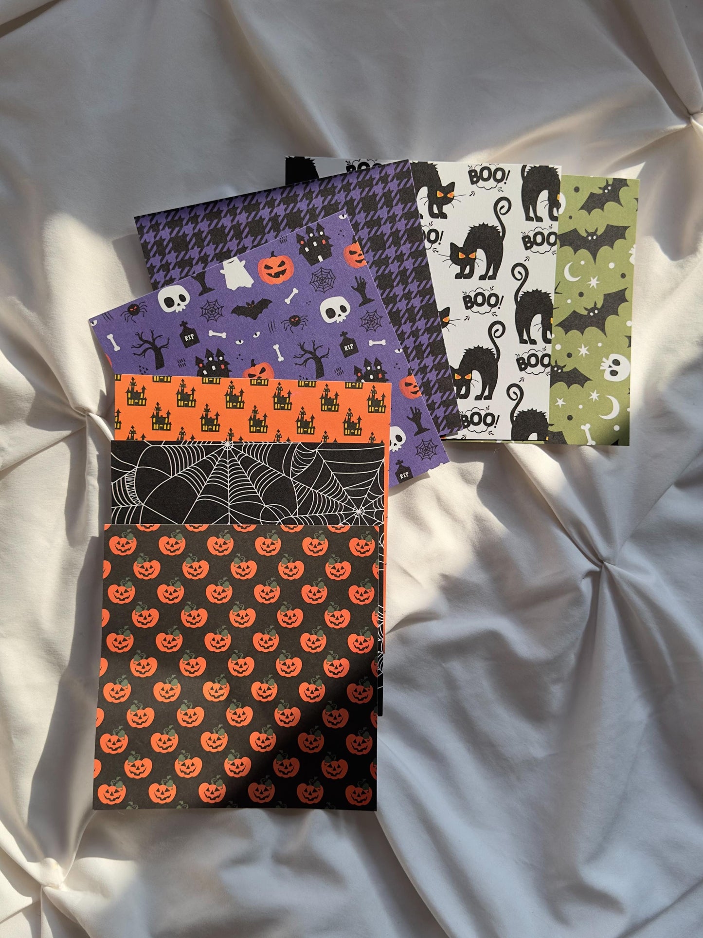 Seven scrapbook papers with different Halloween designs featuring pumpkins, black cats, bats and spiderwebs.