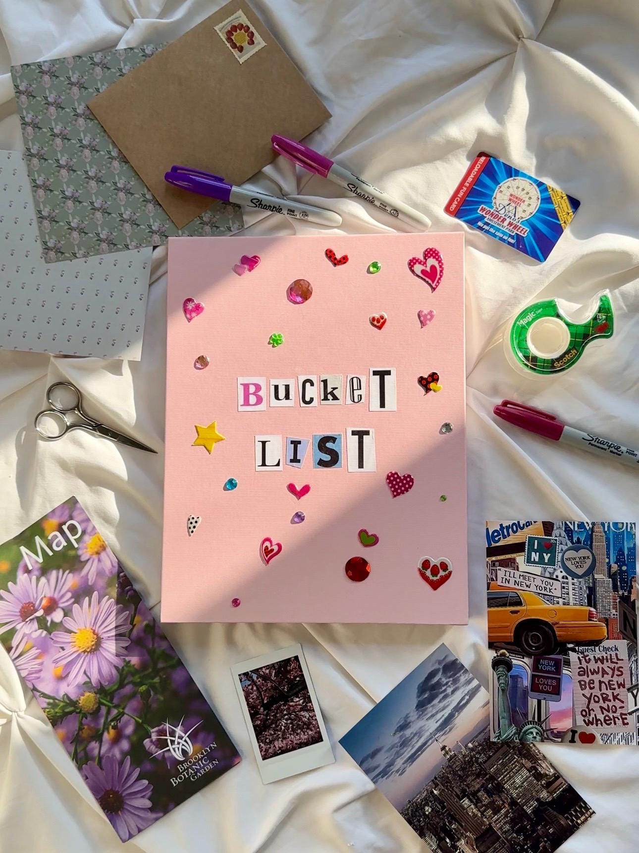 Light pink hardcover scrapbook with “Bucket List” written in newspaper letters. Decorated with heart and star stickers and jewels.