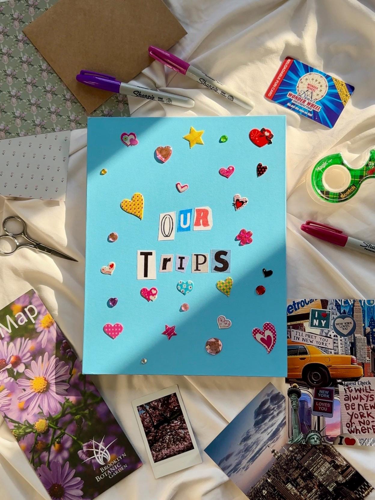 Cobalt blue hardcover scrapbook with our trips in newspaper letters on cover. Decorated with multicolored 3D heart and star stickers and jewels.