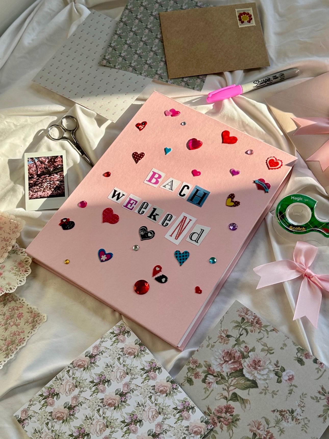 Light pink hardcover scrapbook with Bach Weekend on cover in newspaper letters. Decorated with heart stickers and jewels.
