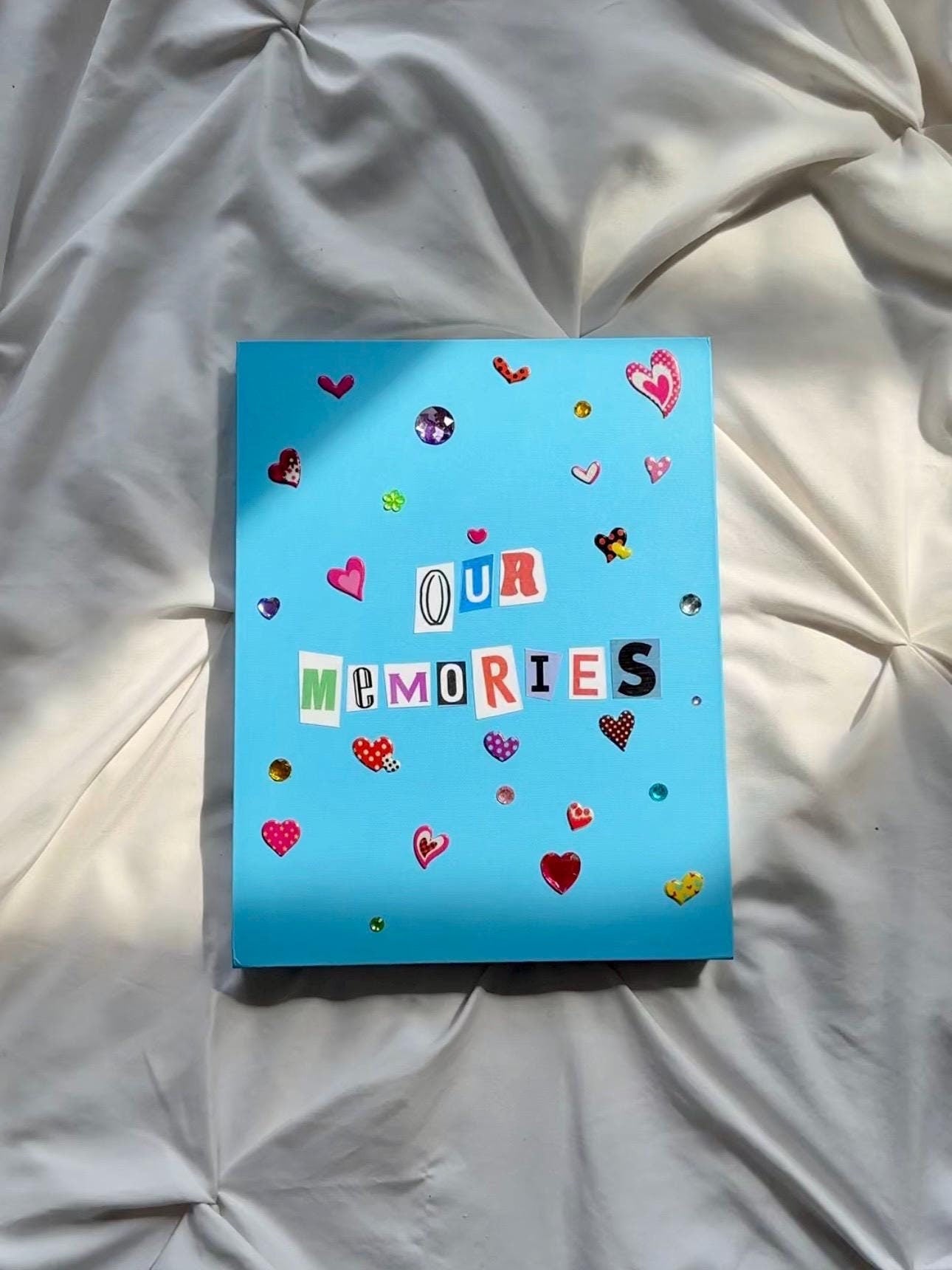 Cobalt blue scrapbook with “Our Memories” written in newspaper letters. Decorated with jewels and heart stickers.