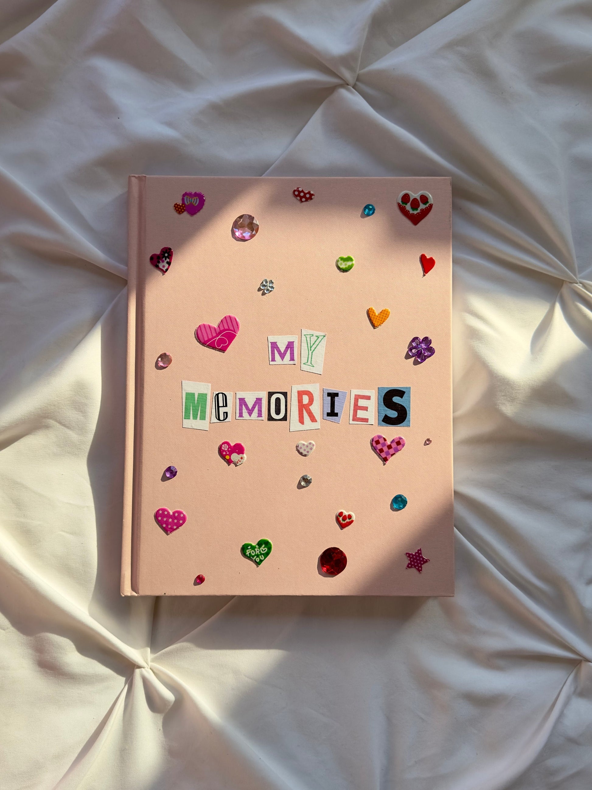 Light pink hardcover scrapbook with newspaper letters spelling my memories on cover. Decorated with puffy heart stickers and jewels.