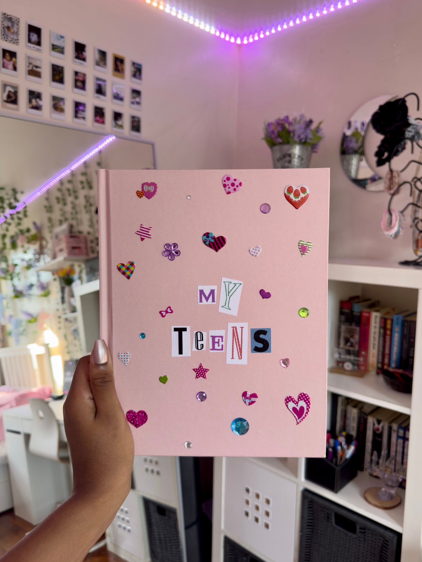 Light pink hardcover scrapbook being held against aesthetic girly bedroom background.