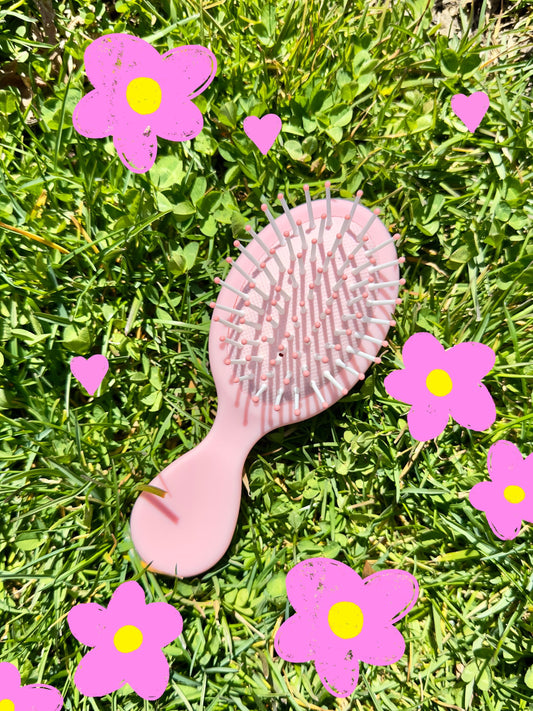 A cute light pink mini brush lying on the grass with pink and yellow flowers.