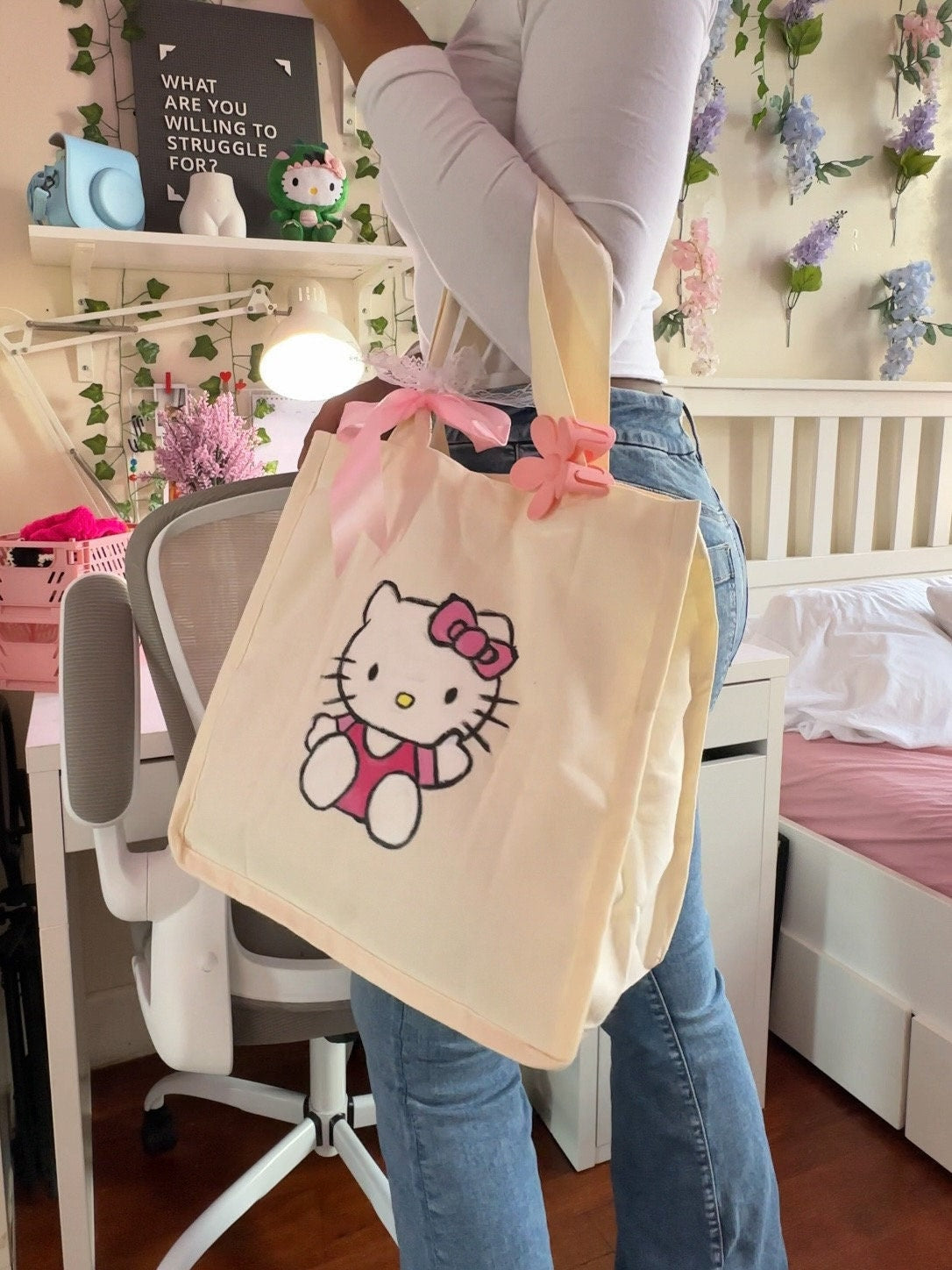 Large beige canvas tote bag with hand painted hello kitty design. Decorated with pink flower hair clip and ribbon bows on handle.