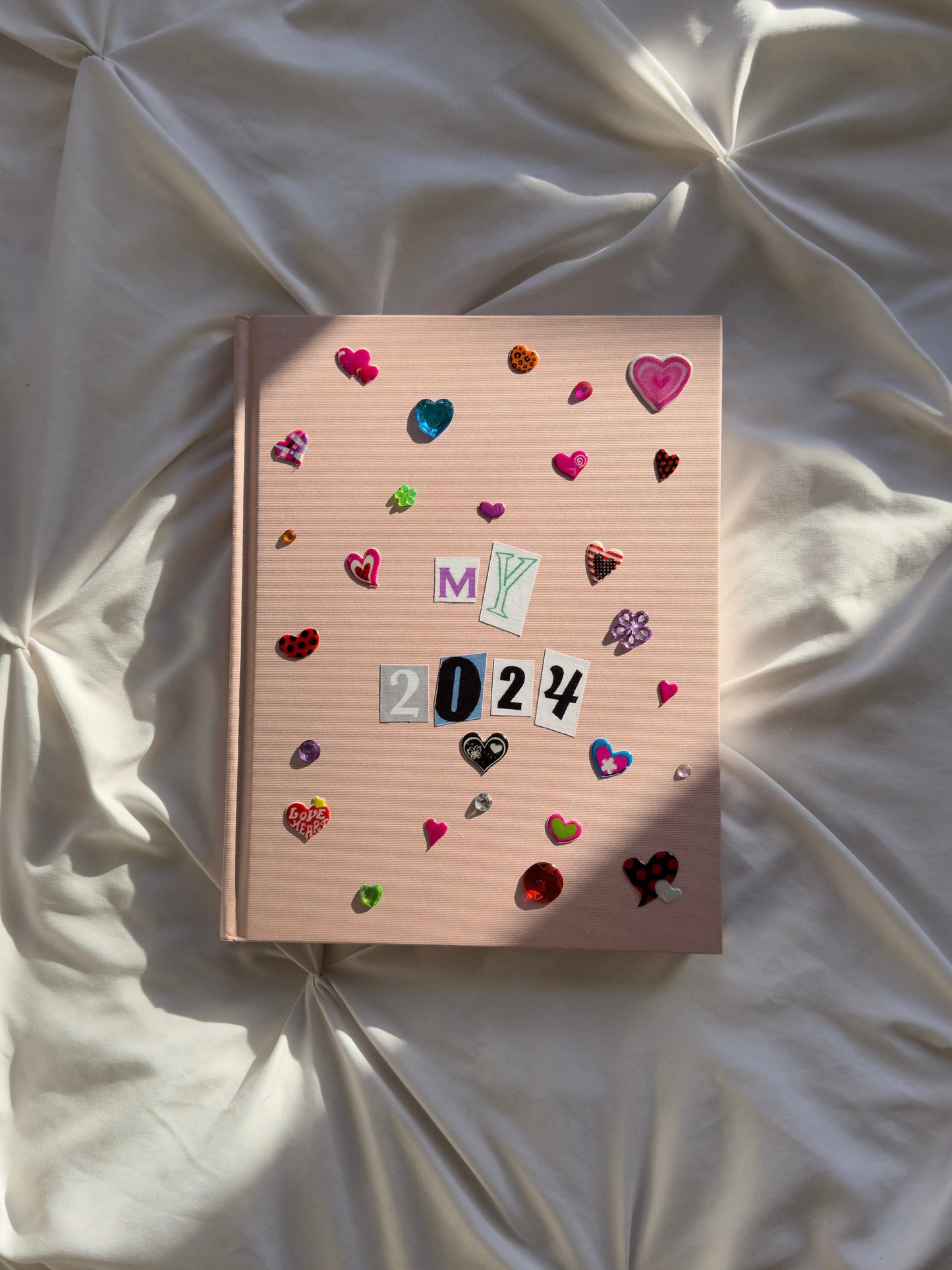 Light pink hardcover scrapbook with My 2024 on cover. Decorated with cute multicolored heart stickers and jewels.