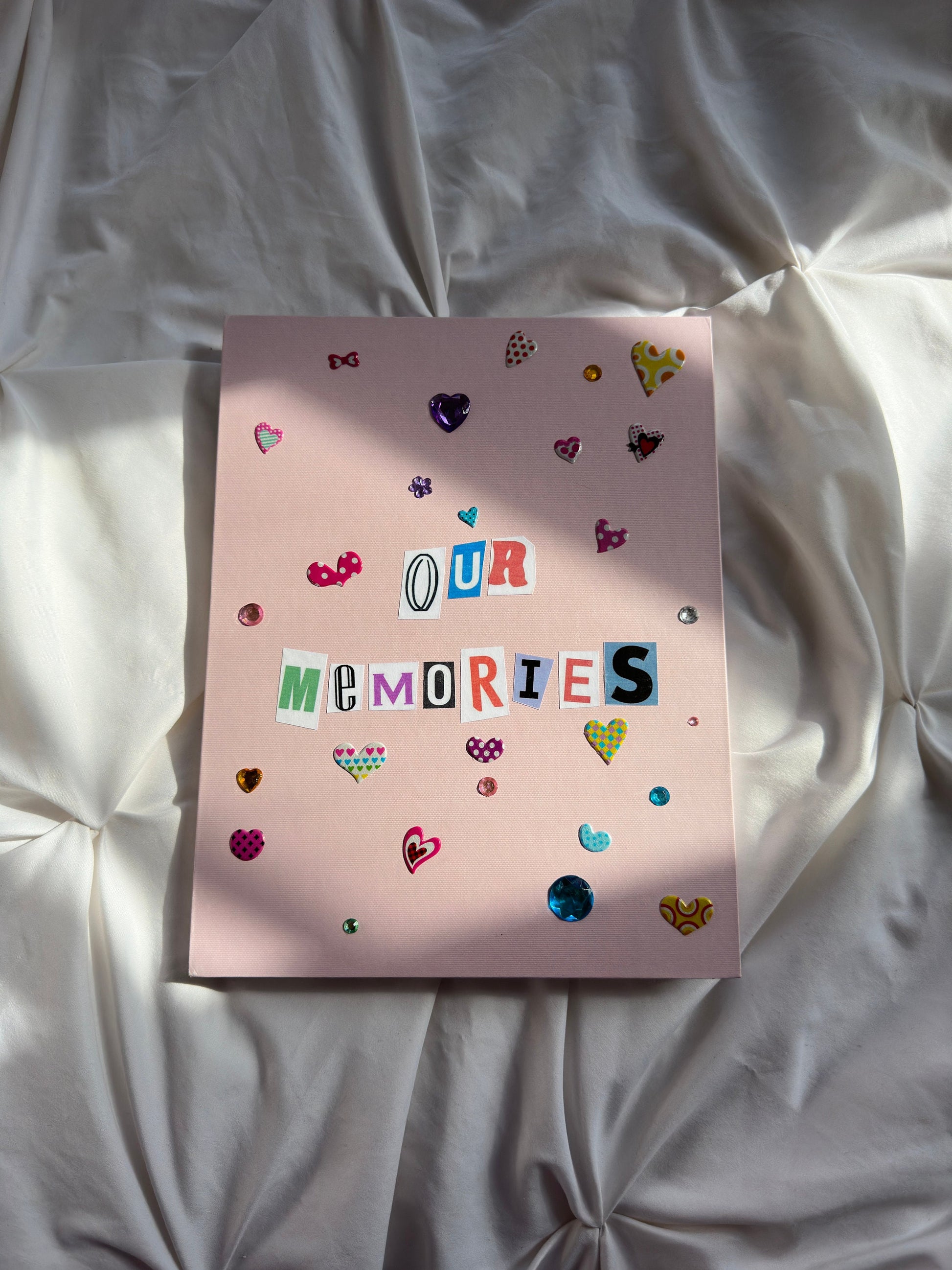 Light pink hardcover scrapbook with “Our Memories” newspaper letters on cover. Decorated with cute heart shaped stickers and jewels.