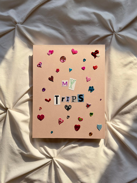 Light pink hardcover scrapbook with My Trips on the cover in newspaper letters. Decorated with cute multicolored heart stickers and jewels.