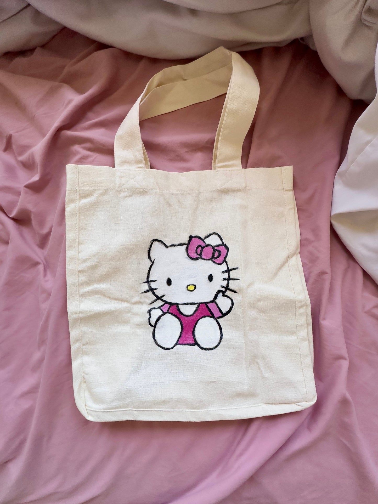 Medium sized beige tote bag with hello kitty waving and dressed pink dress and bow.