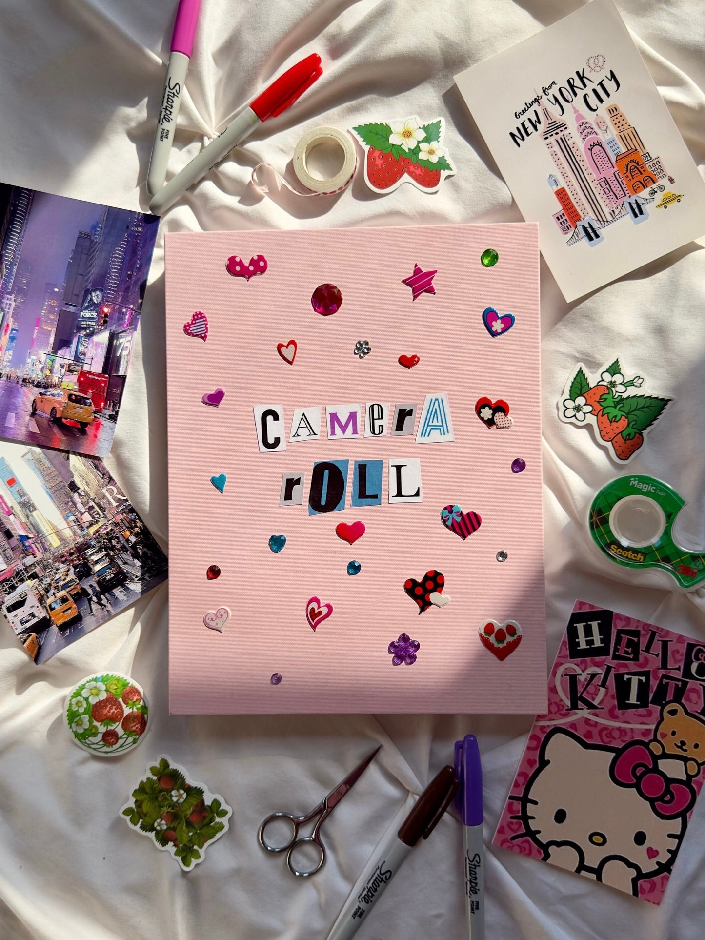 Light pink hardcover scrapbook with “Camera Roll” written in newspaper letters. Decorated with heart and star stickers and jewels.