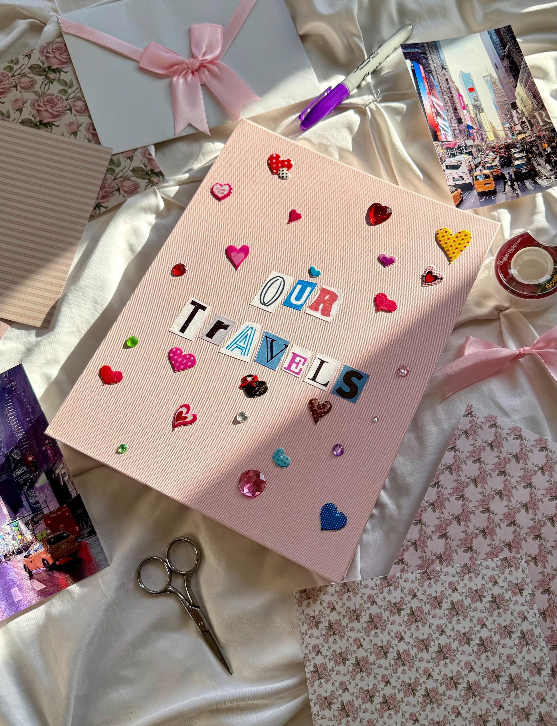 Light pink hardcover scrapbook album with Our Travels on cover in newspaper letters. Decorated with cute heart stickers and multicolored jewels.