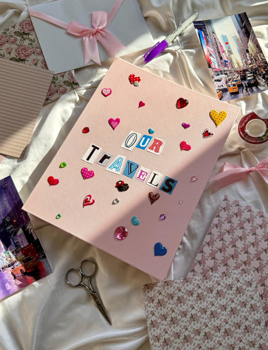 Light pink hardcover scrapbook album with Our Travels on cover in newspaper letters. Decorated with cute heart stickers and multicolored jewels.