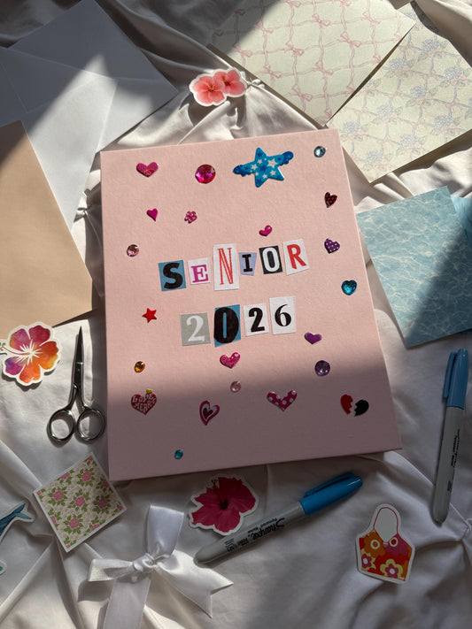 Hardcover light pink scrapbook with newspaper letters reading “Senior 2026”. Decorated with star and heart stickers and jewels.